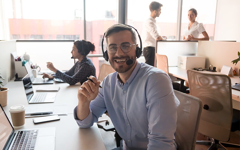 Glimlachende-man-met-headset-achter-computer-in-meeting