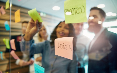 Enthousiaste gebruikers die samenwerken aan een scrumboard met postits en op een agile wijze in overleg zijn