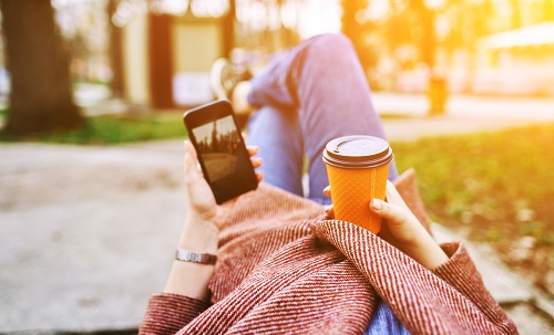 Digitale transformatie, vrouw ligt met mobiele en drinken in gras te genieten van de zon